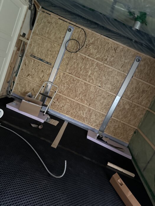 Renoveringsprojekt med uppreglade väggar, OSB-skivor och skenor för skjutdörr, verktyg och material på golvet i ett rum under konstruktion.