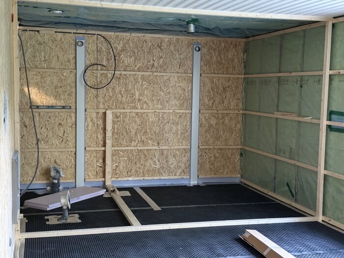 Renoveringsprojekt med uppreglade väggar, ventgolv, och installation av rör och OSB-skivor i rum med grönt isoleringsmaterial på yttervägg.