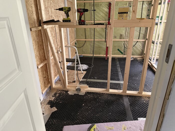 Byggrum med regelverk, golvmaterial och isolering samt verktyg som borrar ligger på en arbetsbänk.