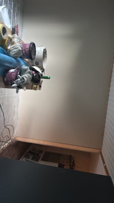 Målade väggar under renovering med färgburkar och måleriverktyg på golvet.