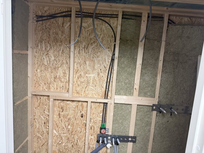 Isolerade väggar med plywood och synliga rör i ett pågående renoveringsprojekt för ett litet badrum.