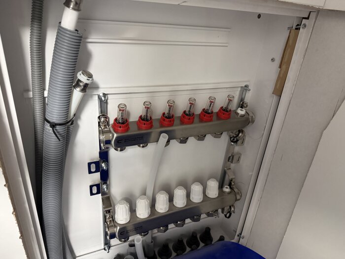 Golvvärmefördelare installerad med kopplade slangar och ventiler, placerad i ett skåp i samband med renovering av badrum.