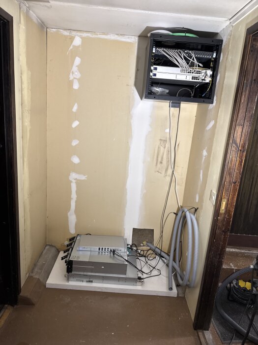 Monterat kabinett och kablar, gipsade väggar med spackelmärken. Slangar och utrustning installerade mot väggen i renoverat utrymme.