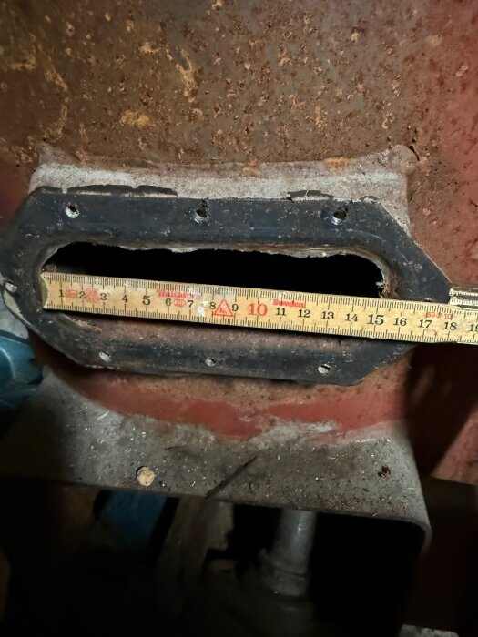 Öppning för elpatron i en gammal panna med ett måttband som visar öppningens bredd, cirka 15 cm, omgiven av rost och slitage.