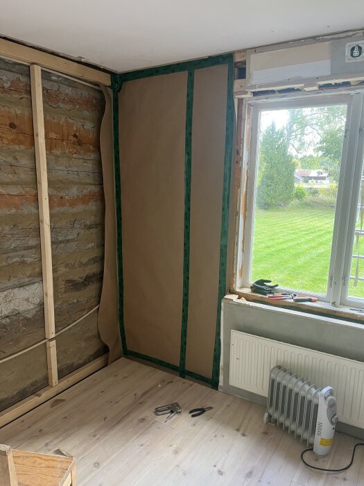 Väggkonstruktion med isolering och ångbroms monterat, ångbromsen fasttejpad. Verktyg på trägolv, fönster bredvid. Konstruktionsprojekt inomhus.