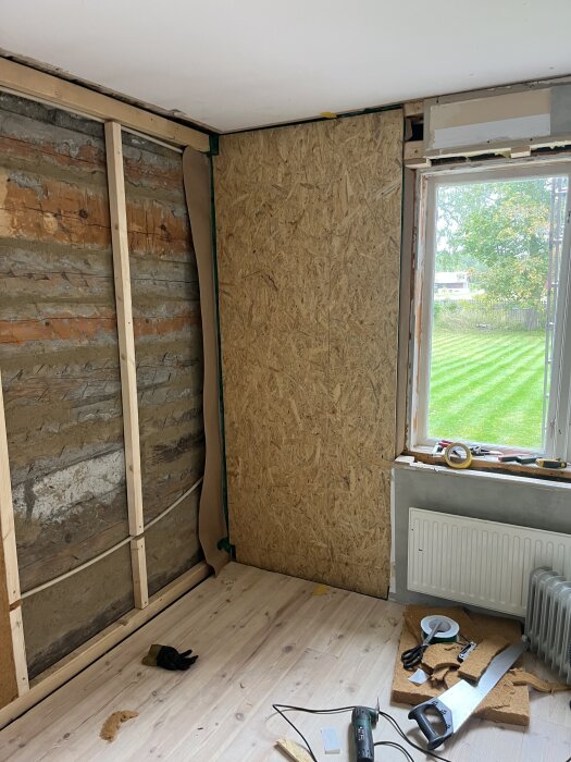 Renovering av vägg i rum med OSB-skiva, synlig isolering och ångbroms. Verktyg och material ligger på trägolvet bredvid ett fönster.