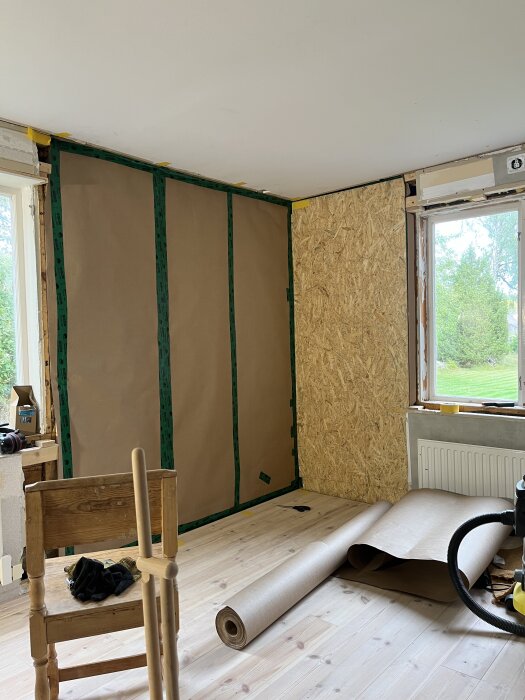 Renoveringsprojekt för vägg med isolering, ångbroms och OSB-skiva. Verktyg och material som pappersrulle och stol i rum med ljust trägolv.