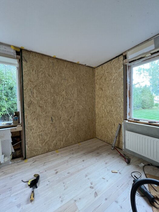 Vägg med obsskiva och ångbroms installerad, verktyg på trägolv och utsikt genom fönster mot trädgård.