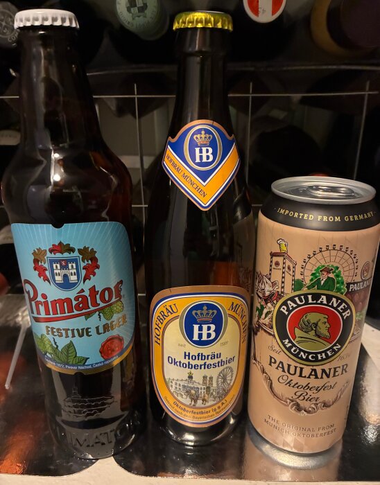 Tre olika ölsorter: Primátor Festive Lager, Hofbräu Oktoberfestbier och Paulaner Oktoberfest Bier på en hylla.