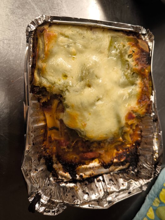 Hemlagad lasagne i en aluminiumform med smält ost och grönsaker på toppen.