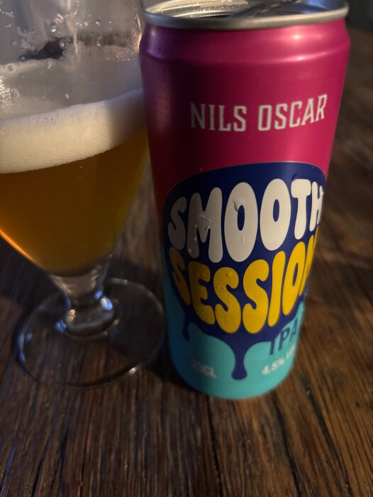 Burk med "Smooth Session IPA" och ett glas öl på ett trätablå.