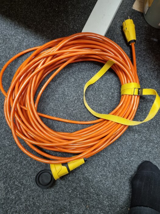 Orange skarvsladd rullad ihop med gula kontakter, placerad på en grå matta.