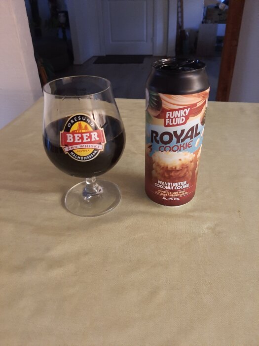 Glas med mörk öl bredvid en burk märkt "Funky Fluid Royal Cookie" på ett bord.