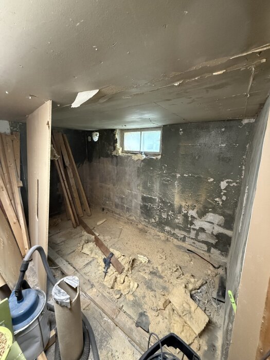 Renovering av källarförråd med synliga isoleringsmaterial, träbrädor och slitna väggar.