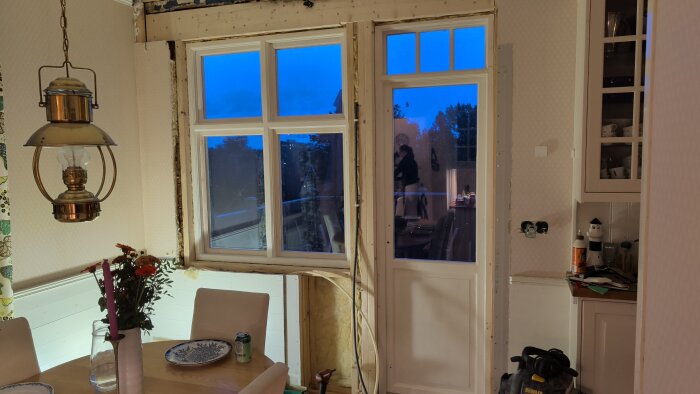 Nytt fönster och altandörr installerade, omgivna av byggmaterial, med en matplats och lampa i förgrunden.