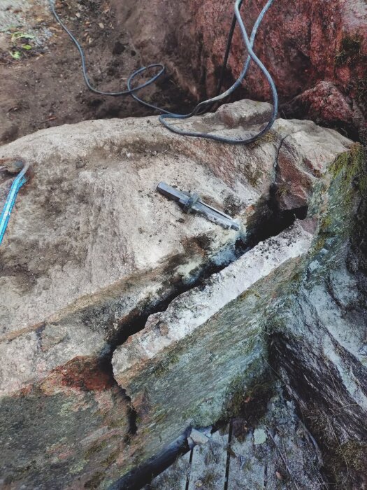 Spricka i bergknalle med verktyg och kablar synliga, där arbetet uppenbarligen pågår för att förbereda ytan för en trallkonstruktion.