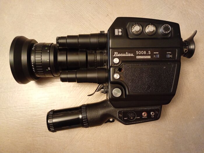 Vintage Beaulieu 5008 S Super 8-filmkamera på ett bord, med flera rattar och linser i metall och svart finish.