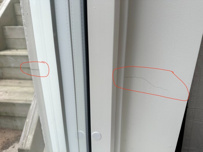 Spricka i en vitmålad yttervägg, markerad med röd cirkel, synlig inomhus vid en dörrkarm, nära utvändigt trappavsnitt.