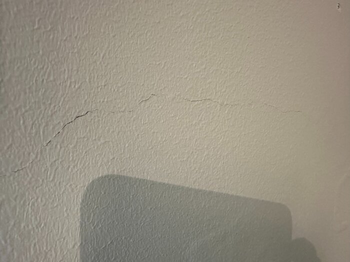 Spricka i väggens färg med ojämn yta, indikerar potentiellt strukturellt problem i källarvåningen av ett nyligen renoverat souterränghus.