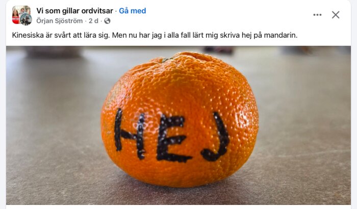 En mandarin med ordet "HEJ" skrivet på ytan i svart bläck, liggande på ett bord.