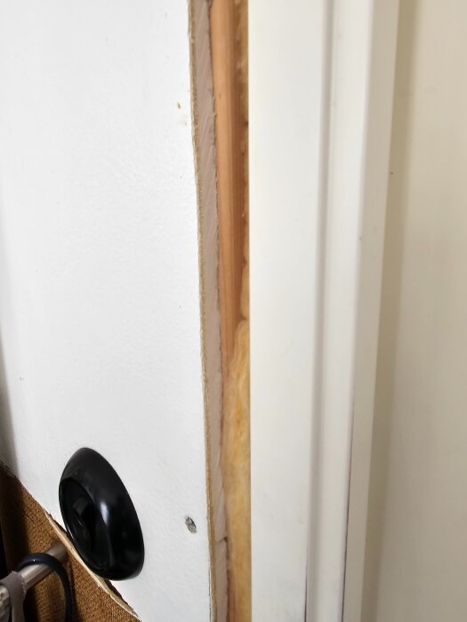 Dörrkarm med synlig nivåskillnad och springa mellan karm och vägg, bröstpanel nedtill, målad vägg upptill.