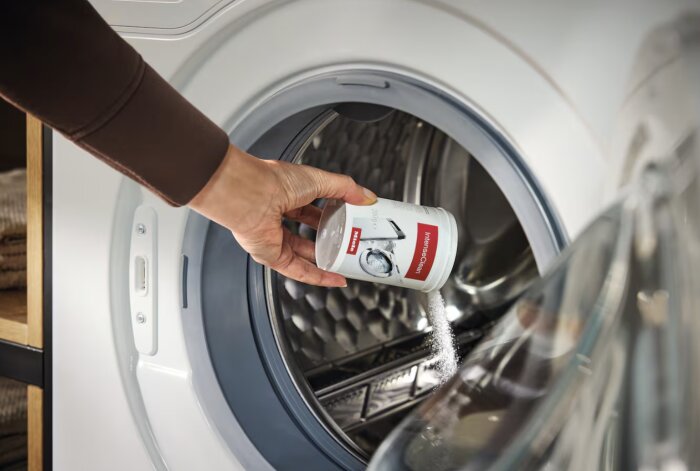 En hand häller IntenseClean rengöringsmedel från Miele i en tvättmaskin.