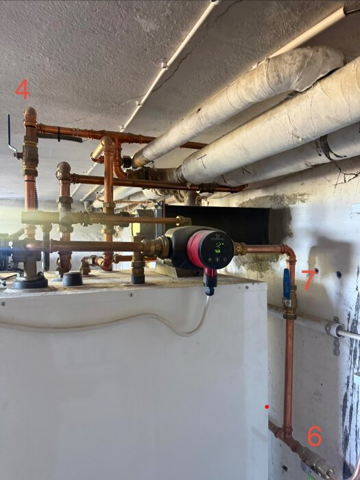 VVS-installation med kopparrör och en cirkulationspump i ett rum med vitmålade väggar och isolerade rör i taket.