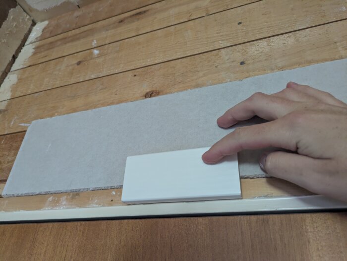 Hand mäter nivåskillnad mellan gipsskiva och dörrfoder, visar en glipa mot träpanel.