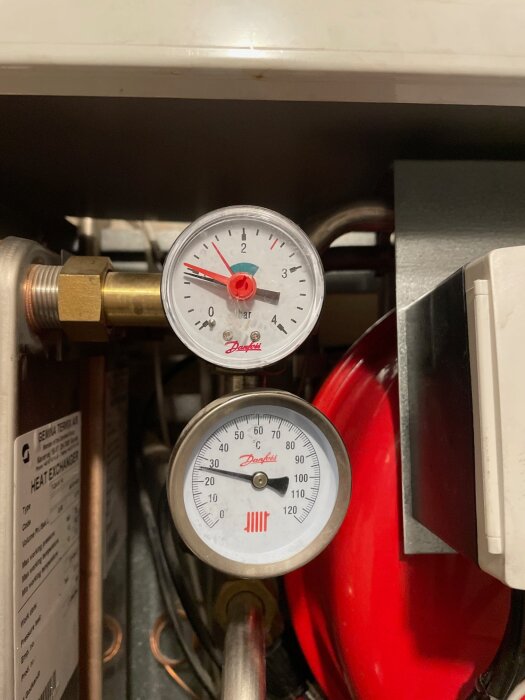 Två tryckmätare i ett rörsystem i en källare, visar mätvärden i bar och Celsius. En del av ett äldre värmesystem i ett radhus.