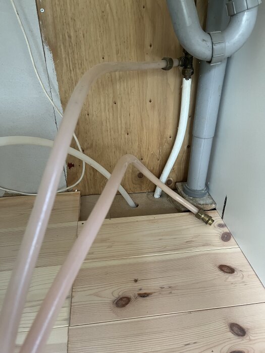 Gamla plastslangar kopplade till ett rörsystem under diskbänk, där ett byte till mer flexibla slangar övervägs.