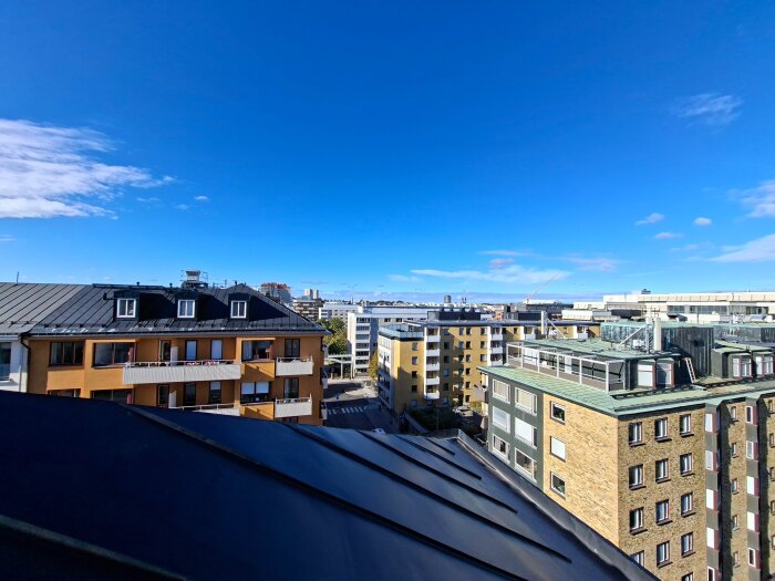 Utsikt över stad från tak med flera flerbostadshus under klarblå himmel.