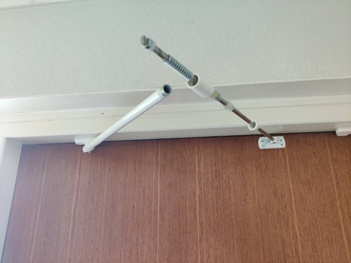 Dörr med installerad dörrbroms i metall och plast, monterad mellan dörrens överkant och dörrkarmen.
