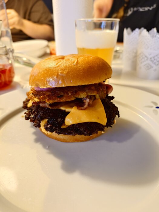 Hemmagjord Piteburgare med picklad rödlök, lingonmayo, bacon och smashad potatisbulle, serverad på en tallrik.