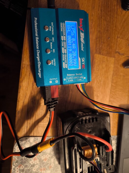 IMAX B6 Mini professionell laddare som laddar ett batteri, anslutet med olika kablar på ett träbord.