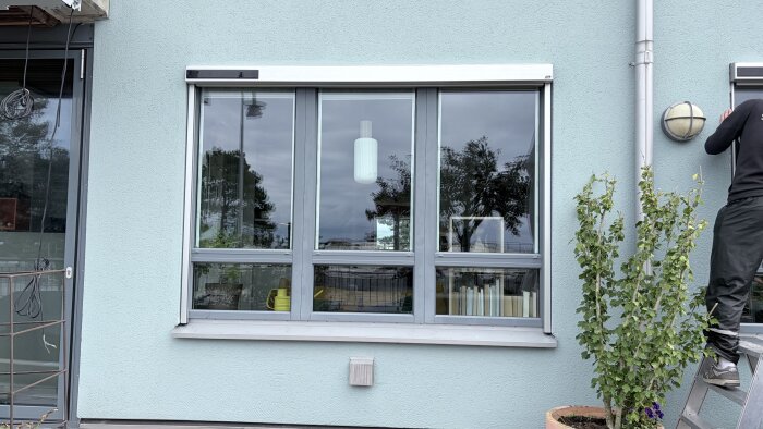 Solcellsdriven zip screen från Luxaflex monterad på fönster, omgivningen speglas i glaset.