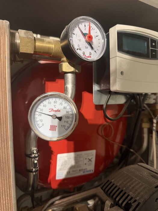 Tryckmätare och termometer på en värmeanläggning med Danfoss-reglering; tryck på 1,5-1,6 bar och temperatur runt 25 °C.