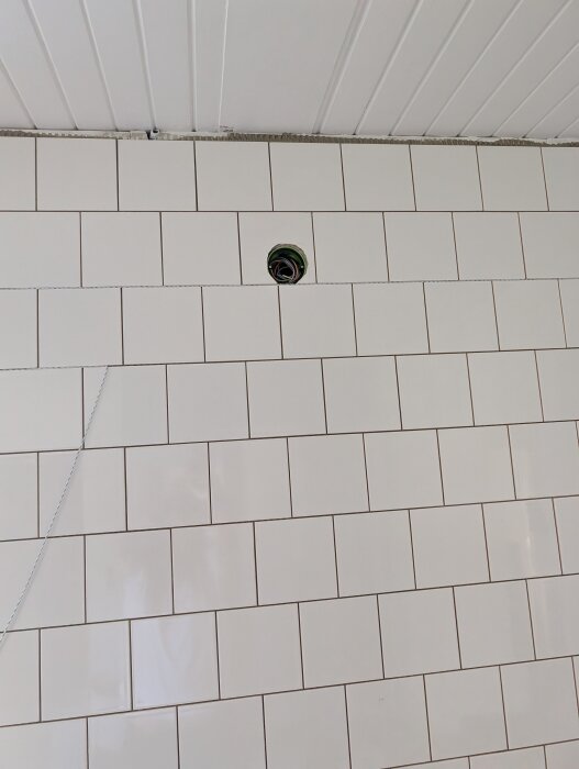 Vit kakelvägg med ett ovalt hål där kablar sticker ut, placerat mitt i kaklet.