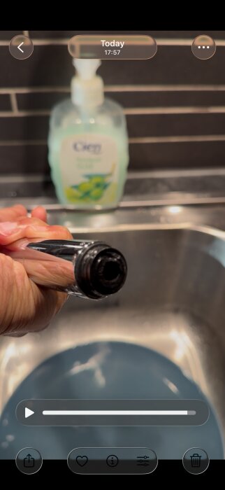 Hand håller en köksblandare med trasig pipnippel ovanför en diskho, handtvål syns i bakgrunden.