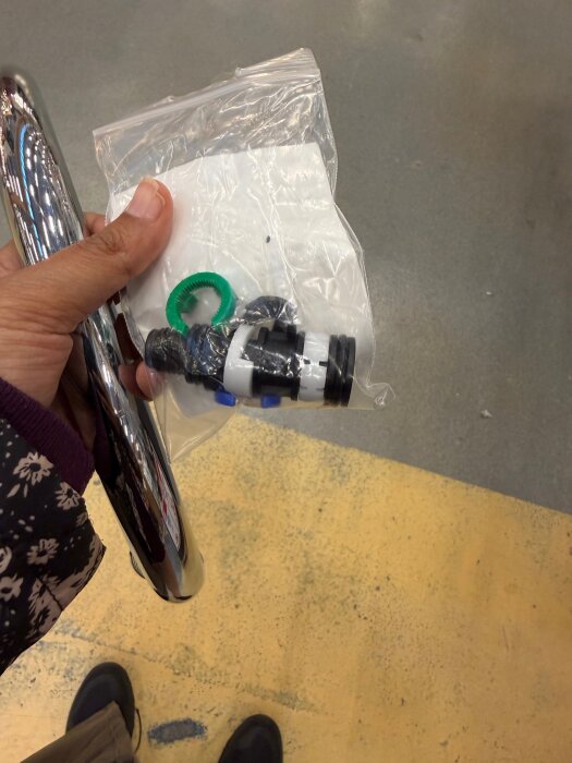 Person håller reservdelar och en köksblandare i handen, delarna är i en plastpåse.