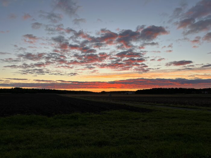 Morgonhimmel med rödorange soluppgång över ett fält och molnig himmel.