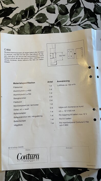 Manual för Contura C850 fläktinstallation med materiallista och monteringsanvisningar på ett bord med bladmönster.