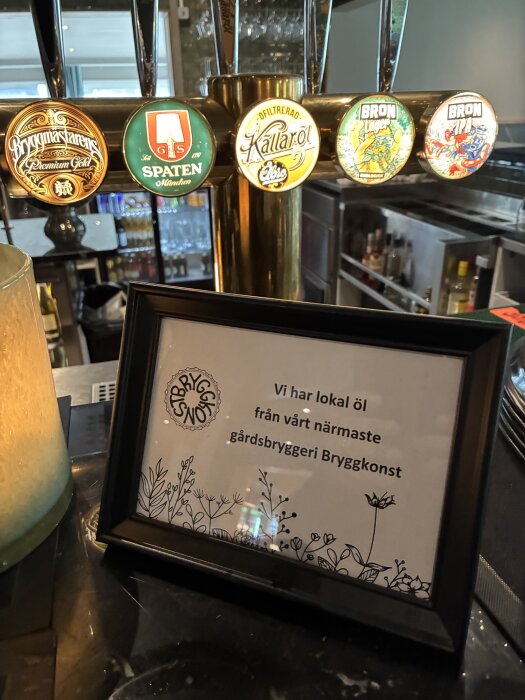 Ölkranar med lokala, bryggda ölsorter och en skylt med meddelandet "Vi har lokal öl från vårt närmaste gårdsbryggeri Bryggkonst" på en bardisk.