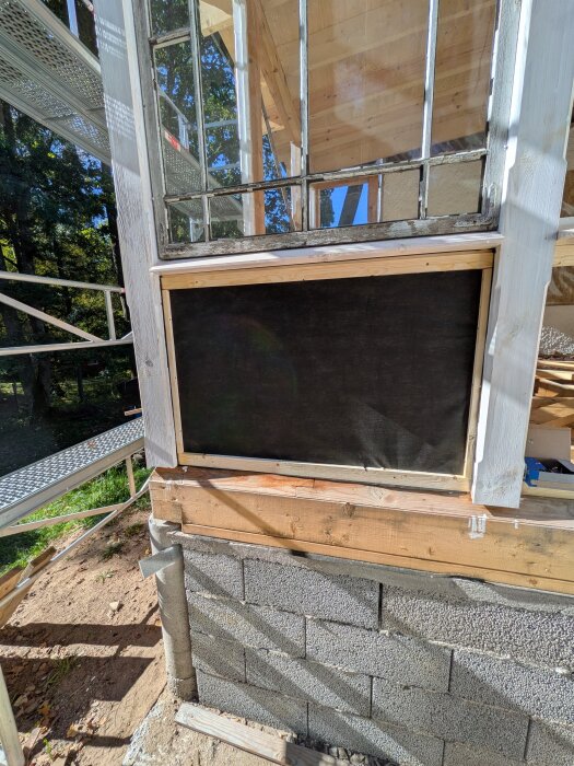 Byggprojekt med trä- och glasfönsterdetaljer, svart duk i luftspalt. Nära isolerad gammaldags veranda med armerade betongblock.