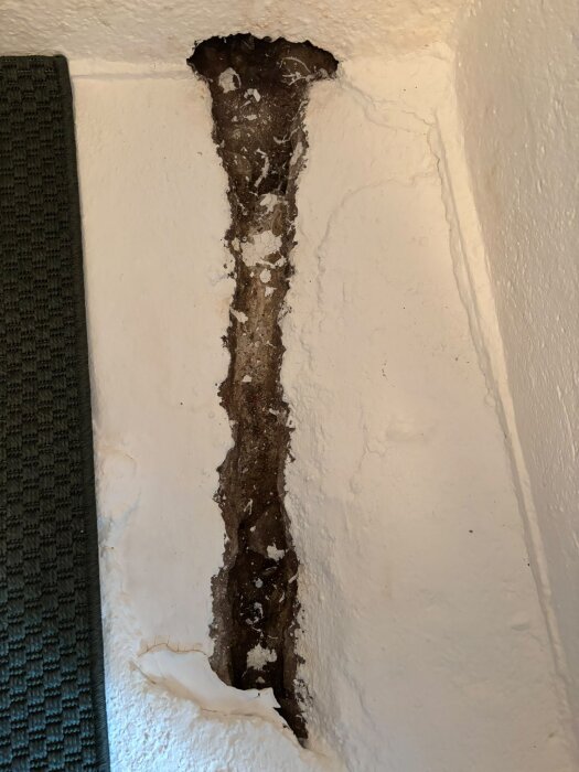 Dike i källarvägg med avskavd färg och fukttecken, delvis synligt rör, tidigare plats för pelletsförråd i ett litet utrymme.
