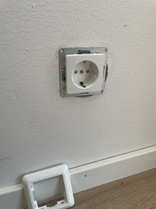 Eluttag monterat utan ram, synlig glipa runt uttaget för att byrå ska stå nära väggen. Ramen ligger på golvet.