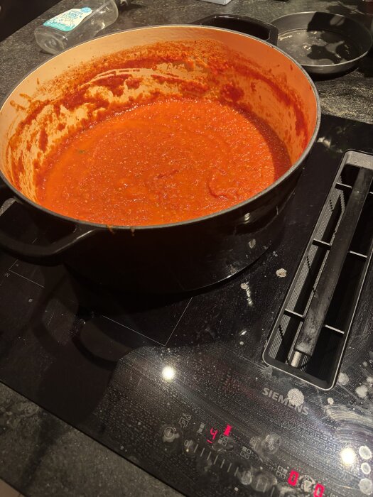 Tomatsås kokar i en stor, svart gryta på en spis.