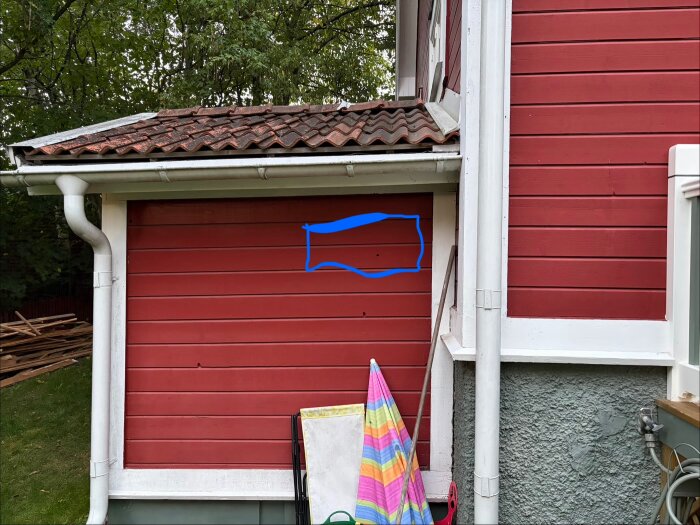 Röd fasad med vita detaljer och sluttande tak. Blå rektangel markerar plats för FTX-installation. Rör och träpanel syns tydligt.