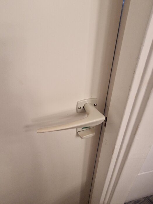 Dörrhandtag i plast med tillhörande roddarpinne, monterat på en vit dörr från ett hus byggt 1967, besvärligt att hitta reservdelar.
