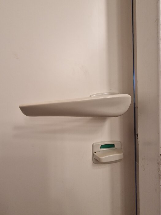 Bilden visar ett vitt, gammaldags dörrhandtag av plast på en vit dörr från 1967. Handtaget har en fast roddarpinne på 7mm.
