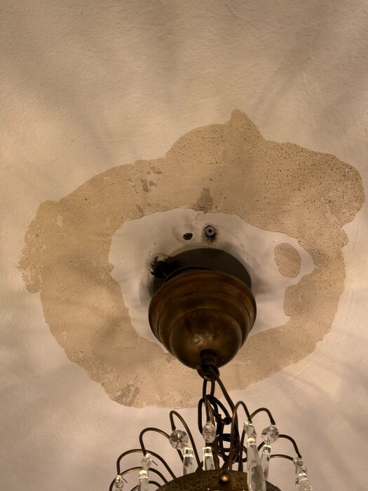 Skadat tak runt lampinfästning med borttagen färg och exponerat underlag, vilket visar behov av reparation och eventuellt spackelarbete.